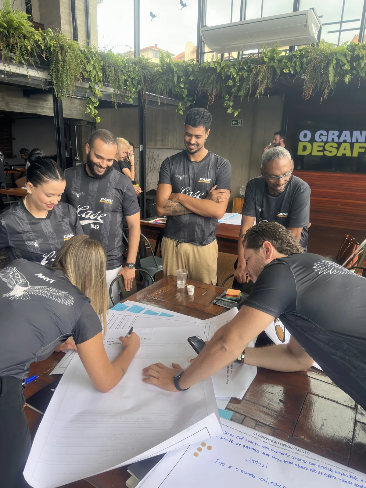 Participantes reunidos ao redor de uma mesa durante uma dinâmica de trabalho em equipe
